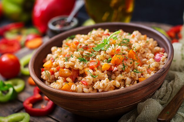 Vegetarian crumbly pearl barley porridge with vegetables  in a dark background