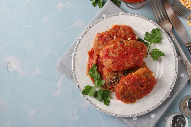 Фото Вегетарианские котлеты из гороха и манной крупы в томатном соусе в тарелке на синей поверхности, вид сверху, копией пространства