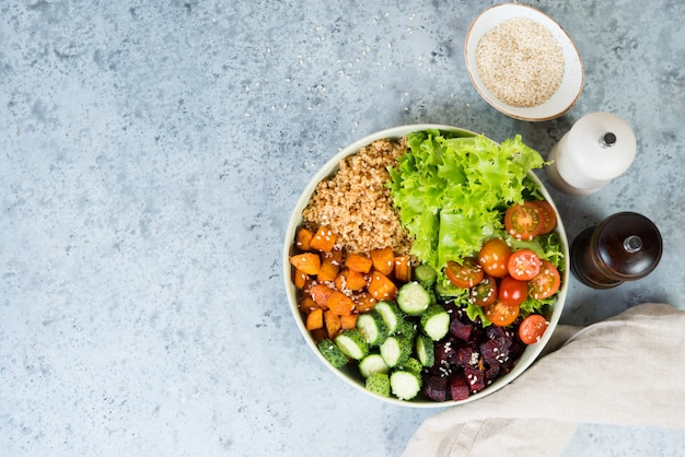 Vegetarian dish a bowl of healthy quinoa with fresh and baked vegetables on a gray concrete background