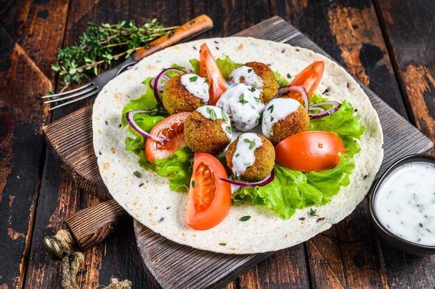 Vegetarian falafel with vegetables and tzatziki sauce on a tortilla bread.