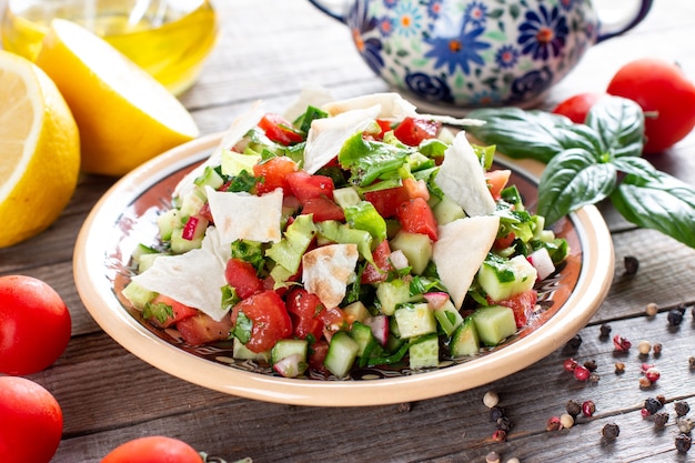 Vegetarian fattoush salad on wooden table. Traditional Middle Eastern salad with toasted pita bread and vegetables. Lebanese cuisine.