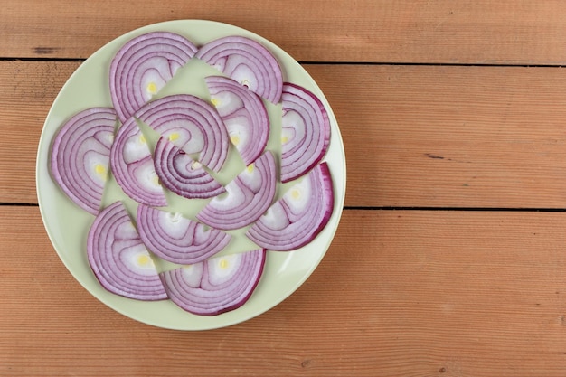 Foto concetto di cibo vegetariano affettato una cipolla viola su un piatto verde su uno sfondo di legno primo piano vista dall'alto