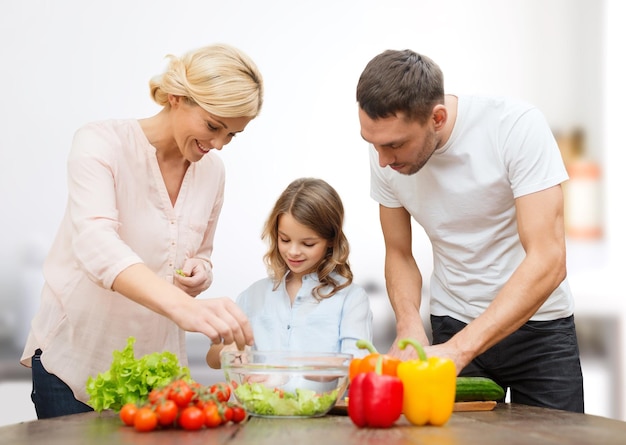 vegetarian food, culinary, happiness and people concept - happy family cooking vegetable salad for dinner over kitchen background