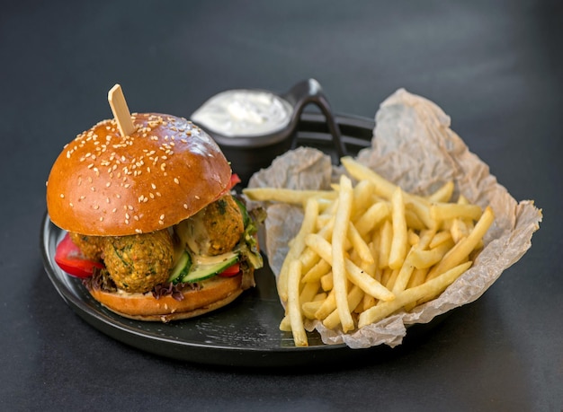 Vegetarian food, fast food burger with falafel and fries on a\
black plate on a black background