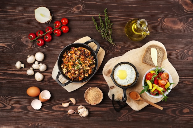 Вегетарианская еда. Жареные грибы и яйца в чугунной сковороде. Ингридиенты для деревенского завтрака на деревянном столе.
