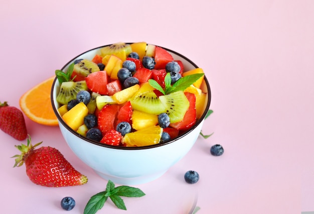 Vegetarian fresh healthy fruit salad on pink table from different fruits.