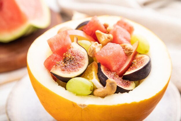 Vegetarian fruit salad of watermelon grapes figs pear orange cashew on white wooden background side view selective focus