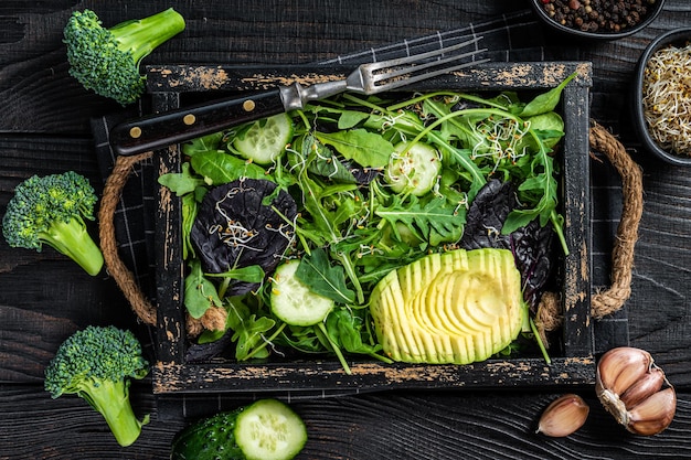 Vegetarian green salad with salad leaves mix avocado and vegetables Black Wooden background Top view