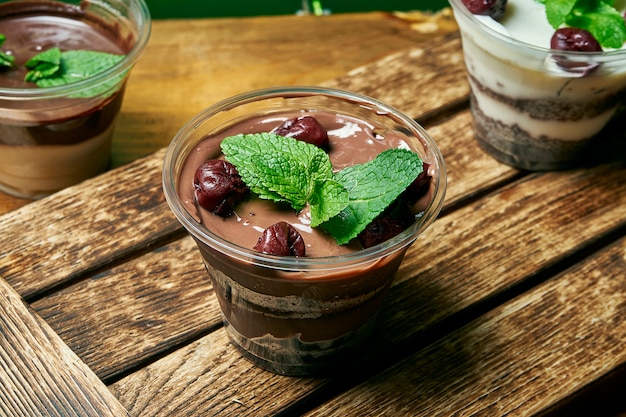 Vegetarian healthy dessert trifle with chocolate and cherry in a plastic container on a wooden table