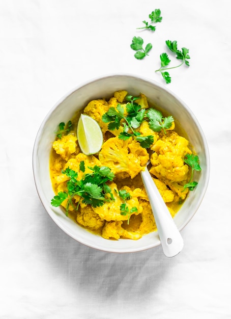 Photo vegetarian indian cauliflower stew with curry sauce cilantro lime on light background top view delicious indian food concept