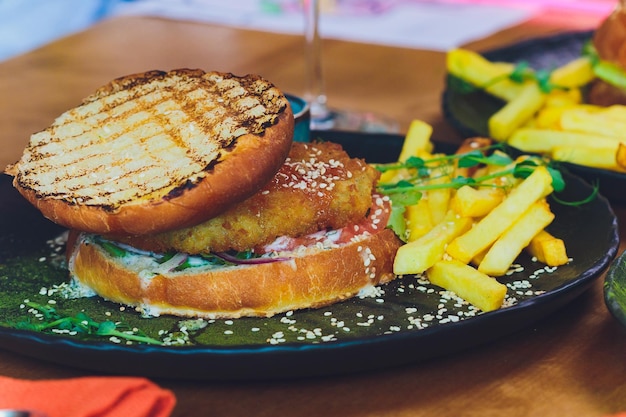 Vegetarian lentil burger in wholewheat bun with lettuce tomato and cucumber accompanied by French fries Selective Focus Focus on the front of the sandwich