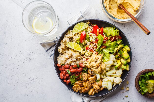 Vegetarian lunch. Brown rice with mushrooms, beans, salad and hummus in black plate, clean eatind.