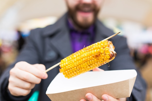 Foto vegetariano e concetto di pasto - bell'uomo che mangia cibo di strada mais al fast food festival