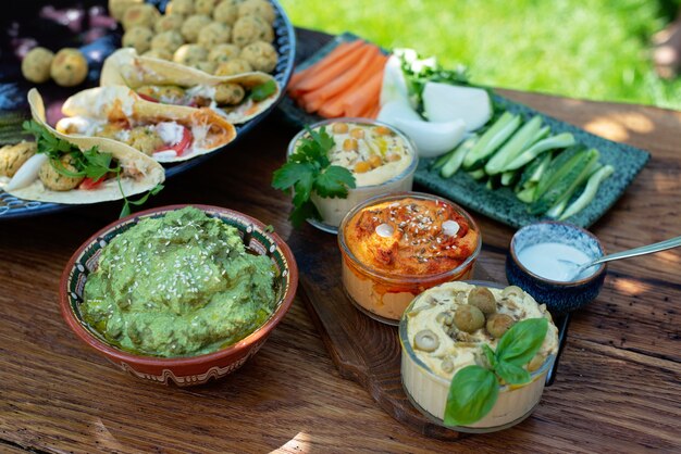 Vegetarian picnic on a wooden oak table, hummus, falafel, pita, vegetables, spinach, basil and sunflower seed pesto sauce. Healthy Mediterranean food.