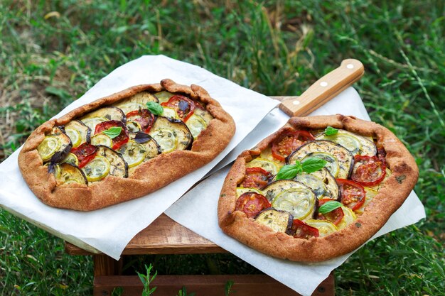 Vegetarian pies with vegetables and herbs on a stool against a background of green grass.