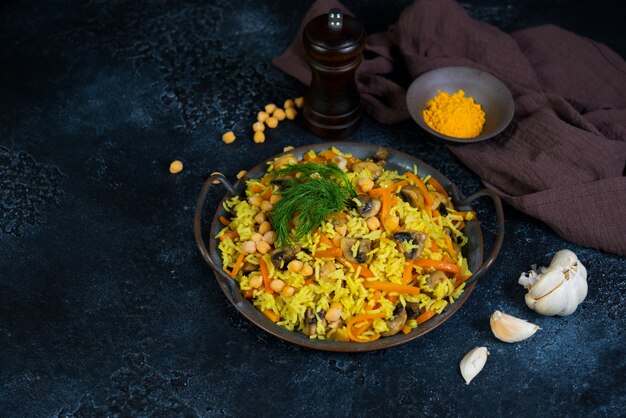 Vegetarian pilaf with mushrooms, vegetables and chickpeas on a black wall. Horizontal photo with copy space.