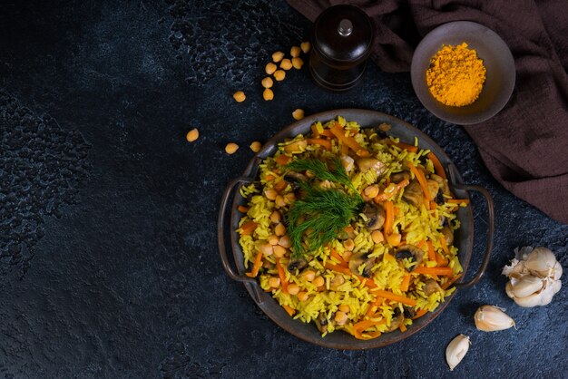 Vegetarian pilaf with mushrooms, vegetables and chickpeas on the right on a black wall. Horizontal photo with copy space. Top view