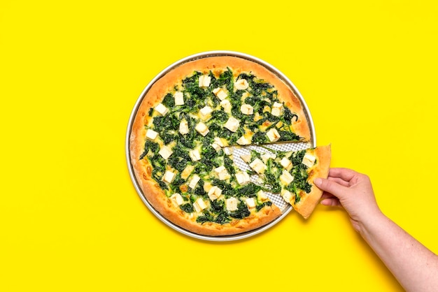 Vegetarian pizza isolated on a yellow background Woman taking a slice of pizza