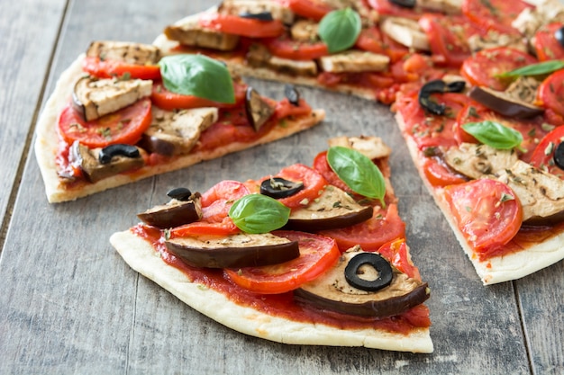 Vegetarian pizza with eggplant, tomato, black olives, oregano and basil on wooden table