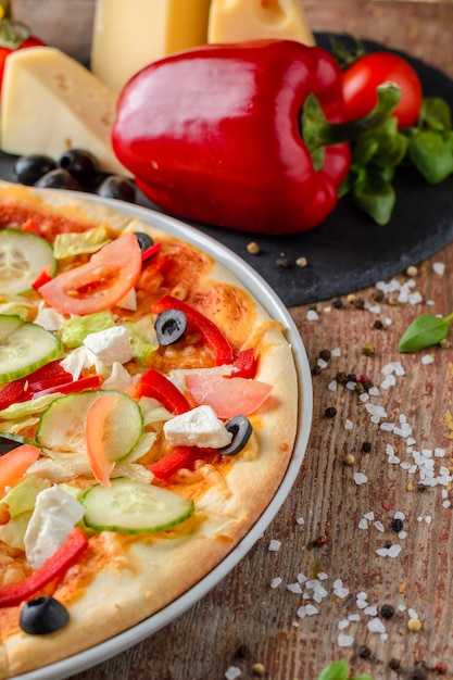 Vegetarian pizza with vegetables and ingredients on a wooden background, close up. Healthy food
