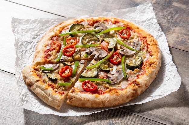 Pizza vegetariana con zucchine pomodori peperoni e funghi su tavola di legno