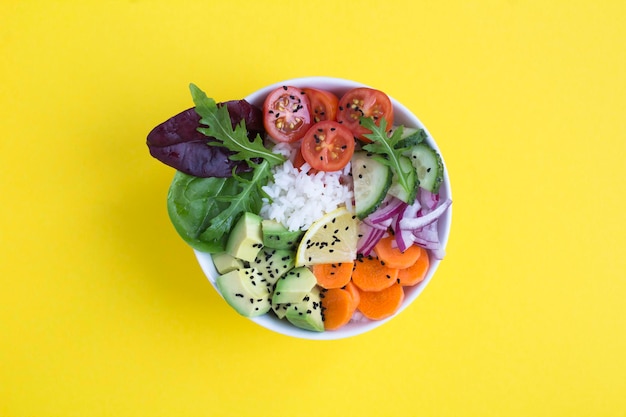Vegetarian poke bowl with rice and vegetable on the yellow  background. Top view. Close-up.