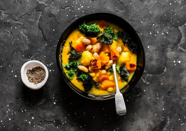 Vegetarian pumpkin potatoes beans and kale stew delicious autumn lunch on a dark background top view