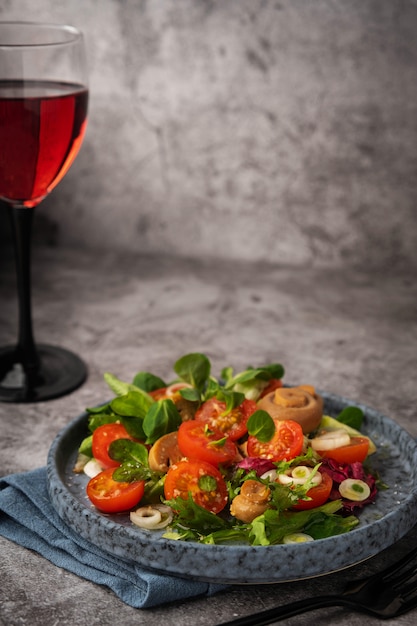 Vegetarian salad of leaves, tomatoes, pickled champignon and glass of red wine on a gray background, copy space