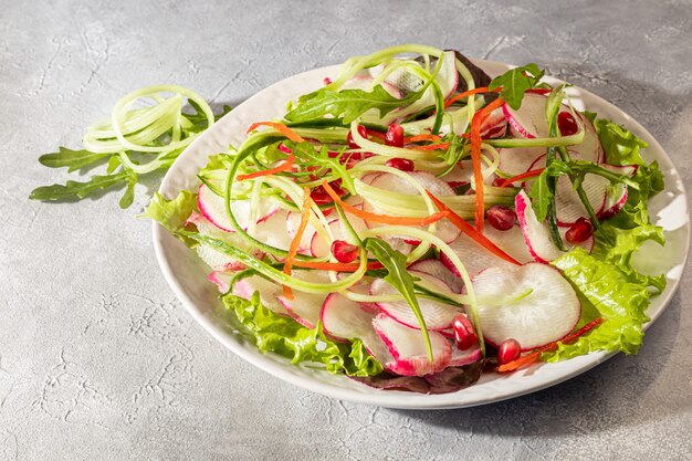 Vegetarian salad of radish, spinach, red onion and bell pepper and cucumber. On a light background. Copy space.