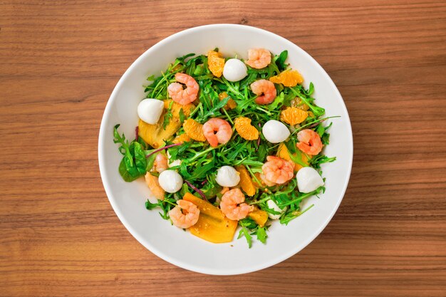 Vegetarian salad with arugula, persimmon, mandarine, shrimps and mozzarella