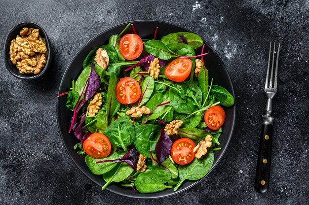 Vegetarian salad with mix leaves mangold, swiss chard, spinach, arugula and nuts in a salad bowl. Black background. Top view.