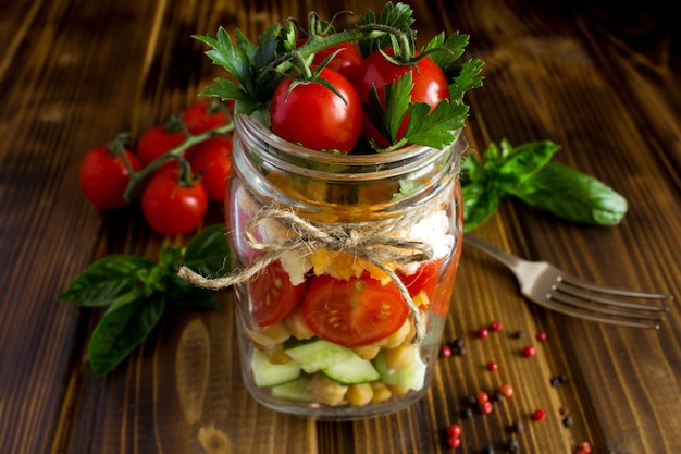 Vegetarian salad with vegetables and chickpea  in the glass jar on the brown wooden  background