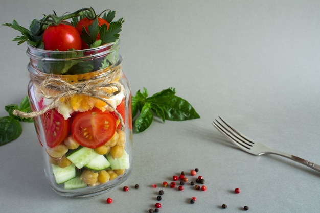 Vegetarian salad with vegetables and chickpea  in the glass jar on the  grey  surface