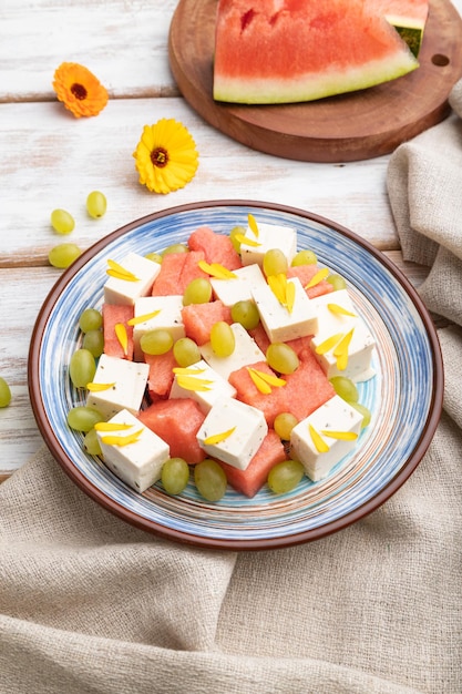 Vegetarian salad with watermelon feta cheese and grapes on blue ceramic plate on white wooden background Side view