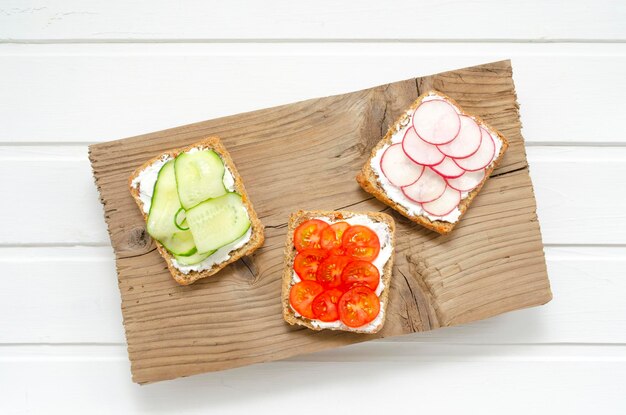 vegetarian sandwiches with cream cheese fresh cucumber radish tomatoes on a board on a white wooden