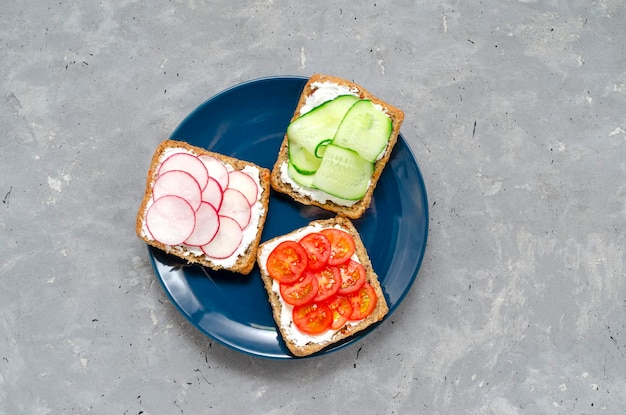 Фото Вегетарианские бутерброды со сливочным сыром, свежими огурцами, редисом, помидорами на тарелке