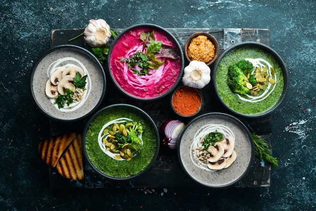 Vegetarian set of soups Beet soup broccoli cream soup and mushroom soup Top view Free space for your text On a black stone background