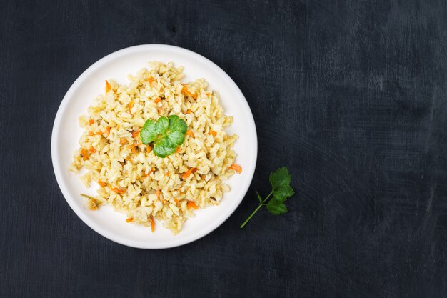 Vegetarian stewed side dish of brown rice with onions and carrots in a white plate on a black