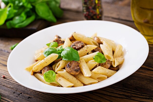 Pasta di verdure vegetariano penne con funghi in ciotola bianca sul tavolo di legno.