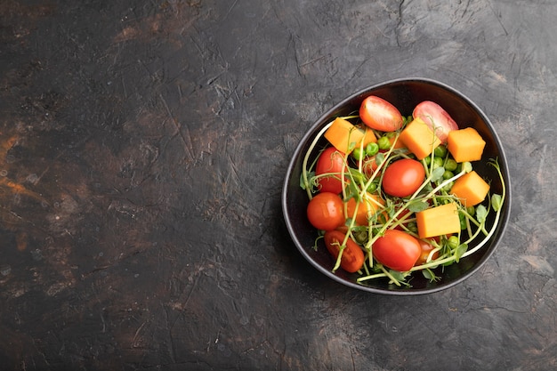 Vegetarian vegetable salad of tomatoes, pumpkin, microgreen pea sprouts on black concrete