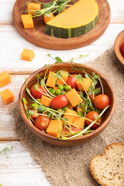 Vegetarian vegetable salad of tomatoes pumpkin microgreen pea sprouts on white wooden background Side view