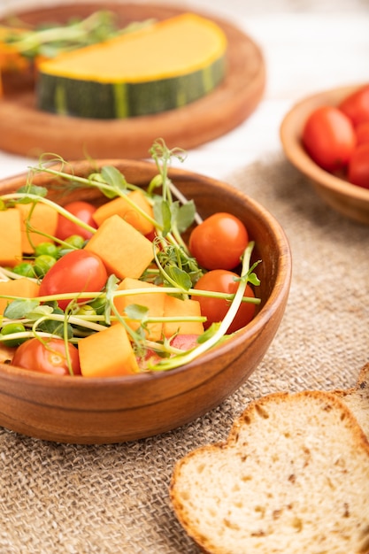 Vegetarian vegetable salad of tomatoes, pumpkin, microgreen pea sprouts on white wooden