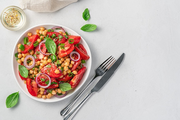 Vegetarian, vegetable salad with chickpeas, tomatoes and fresh herbs on a gray background. Healthy food. Top view, copy space.