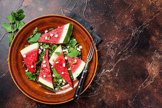 Vegetarian watermelon salad with feta cheese, arugula, onions. Dark background. Top view. Copy space.