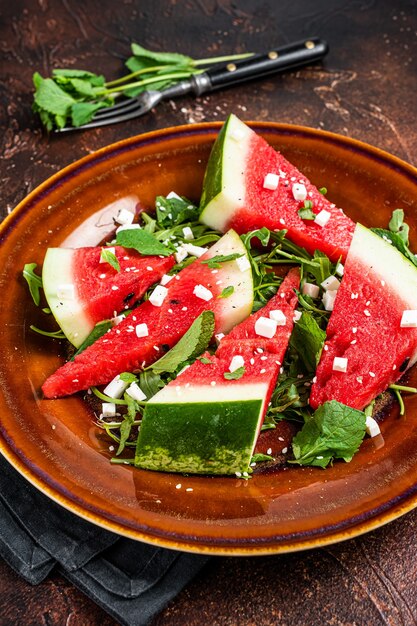 Vegetarian watermelon salad with feta cheese, arugula, onions. Dark background. Top view.