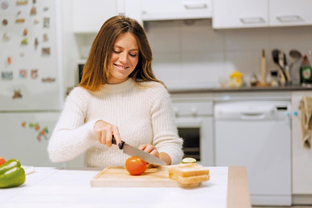 菜食主義者の女性が家庭で野菜のサンドイッチを調理し、トマトのスライスを切る