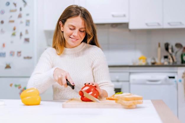 菜食主義者の女性が自宅のキッチンで野菜のサンドイッチを調理し、唐辛子を切る