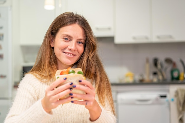 Вегетарианка готовит овощной сэндвич на кухне дома, заканчивая его приготовление