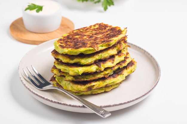 Vegetarian zucchini fritters or courgettes pancakes, served with fresh herbs and sour cream.