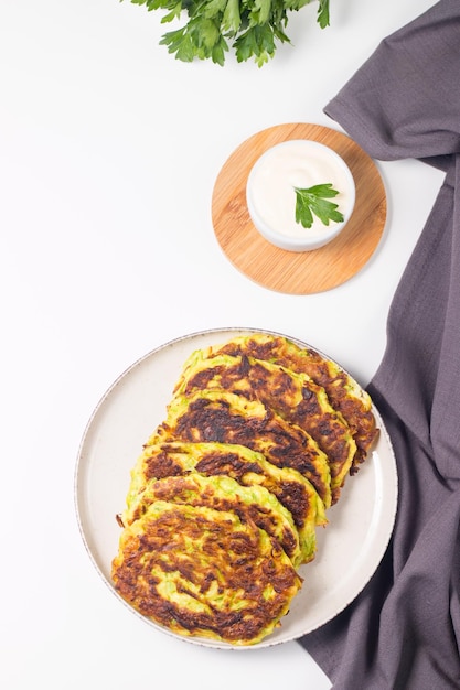 Vegetarian zucchini fritters or courgettes pancakes, served with fresh herbs and sour cream.